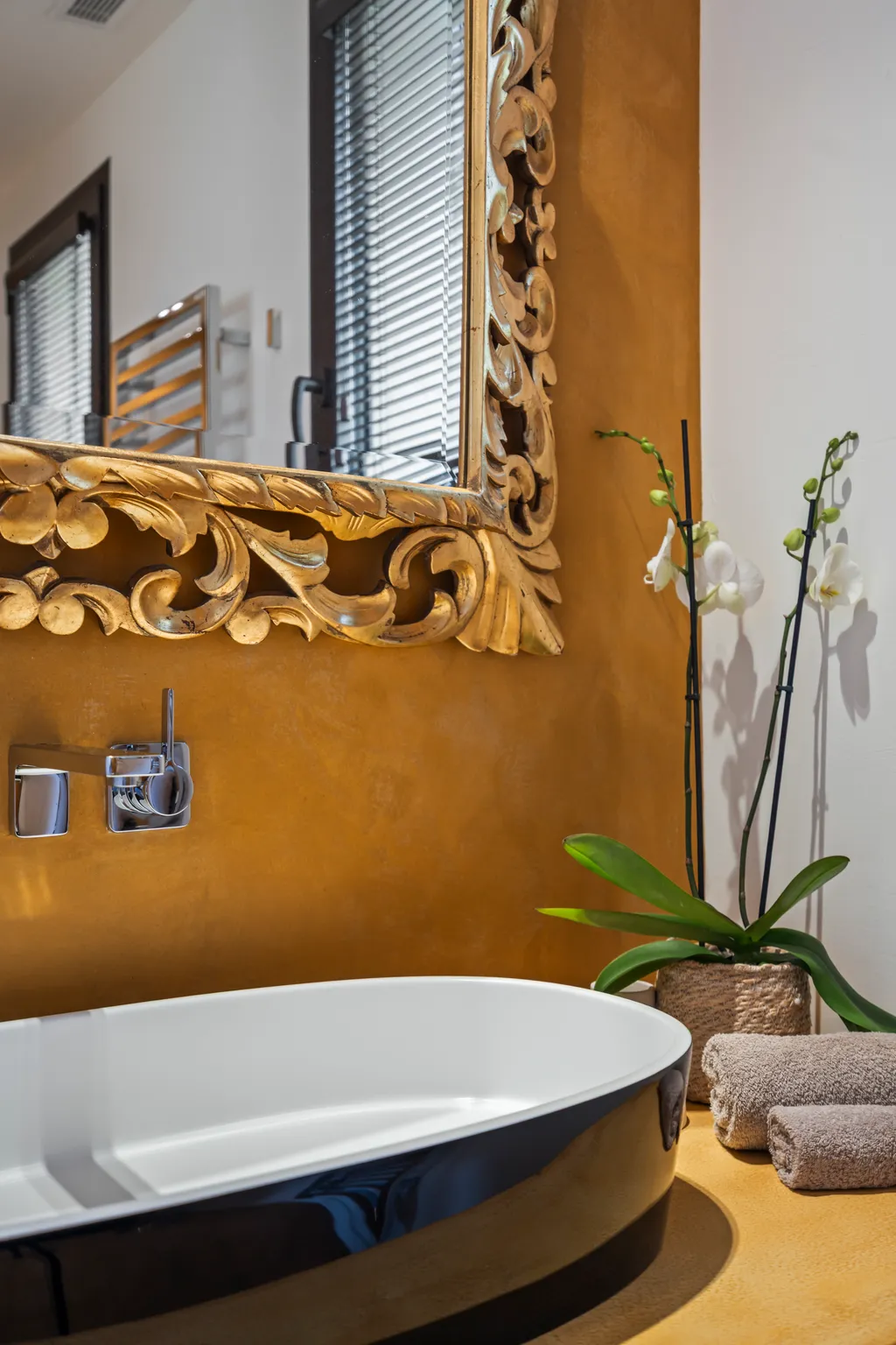The master bedroom's en-suite bathroom — a black oval tub below a carved gilt mirror on an ochre wall