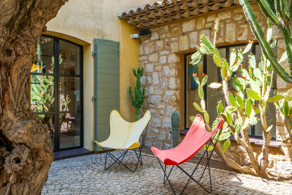 Coral and cream butterfly chairs on a cobbled courtyard against the villa's ochre stone wall