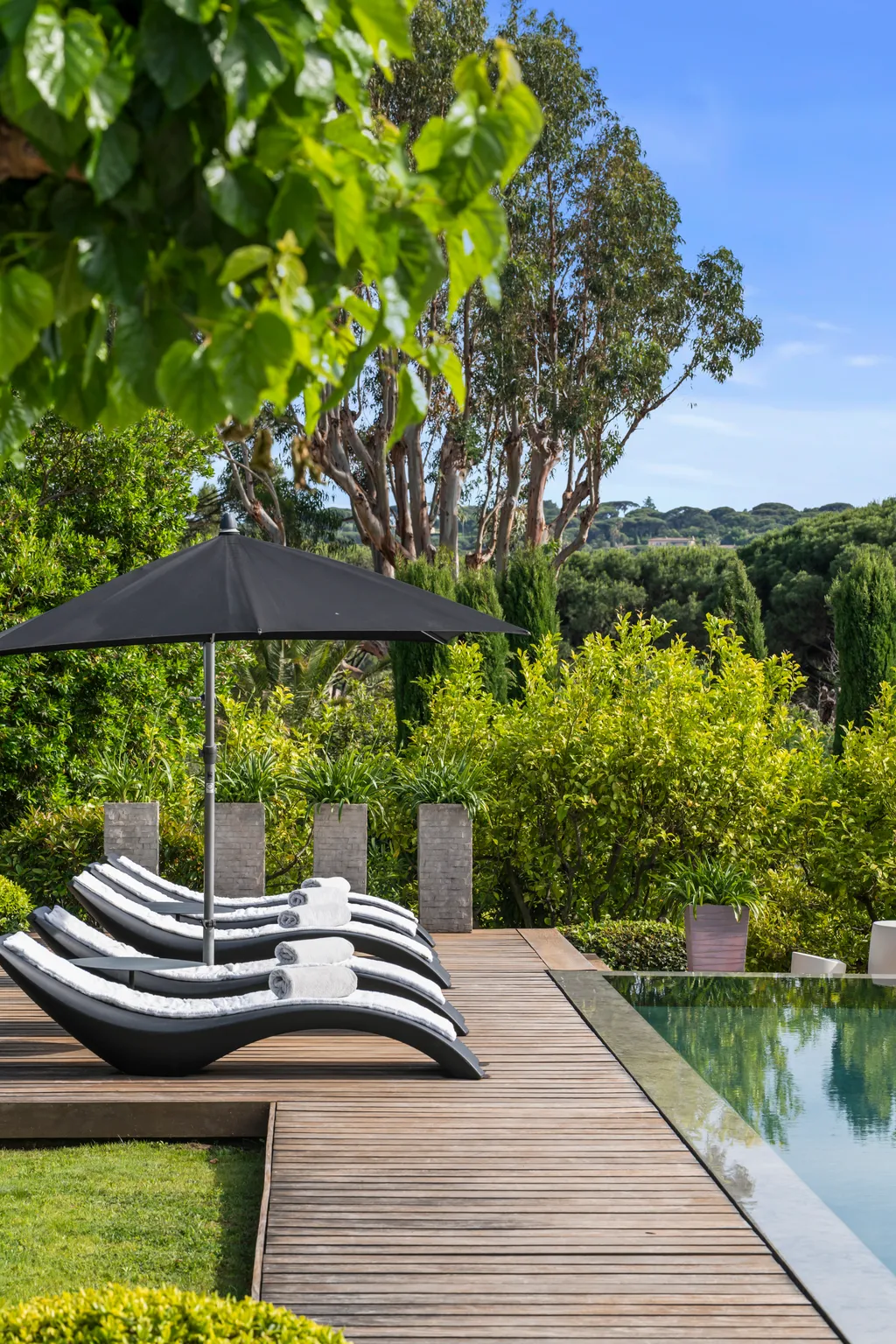 Cushioned loungers with rolled towels on the pool deck, looking out over the garden
