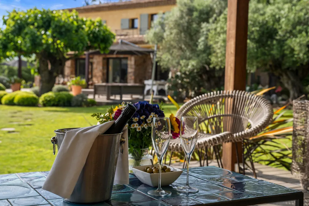 An ice bucket and rosé on a shaded terrace table, the villa's garden beyond