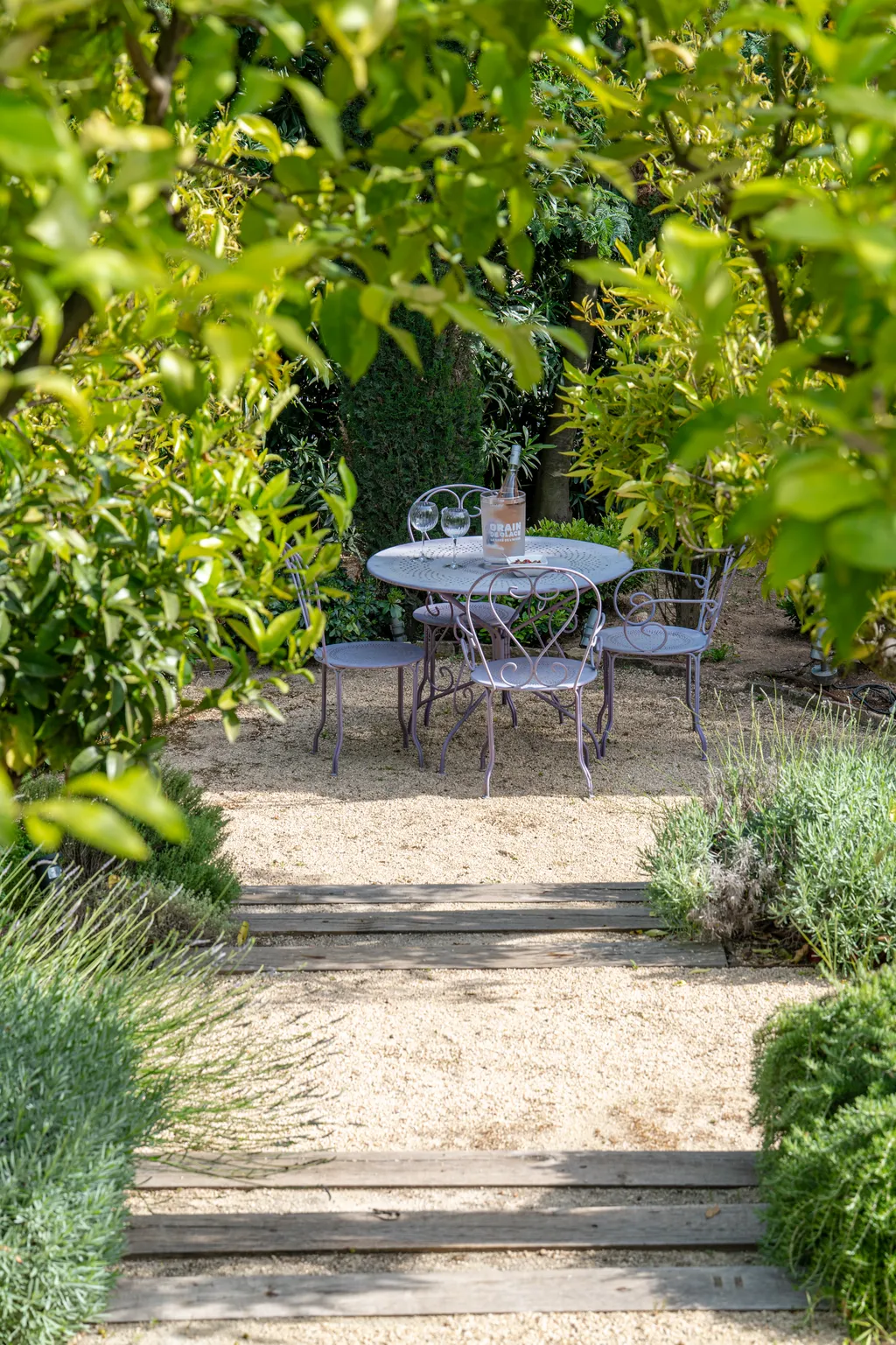 A wrought-iron café table for four on a gravel path, framed by fruit trees