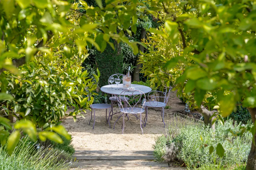 A grey iron garden table among lemon trees and lavender on a gravel path