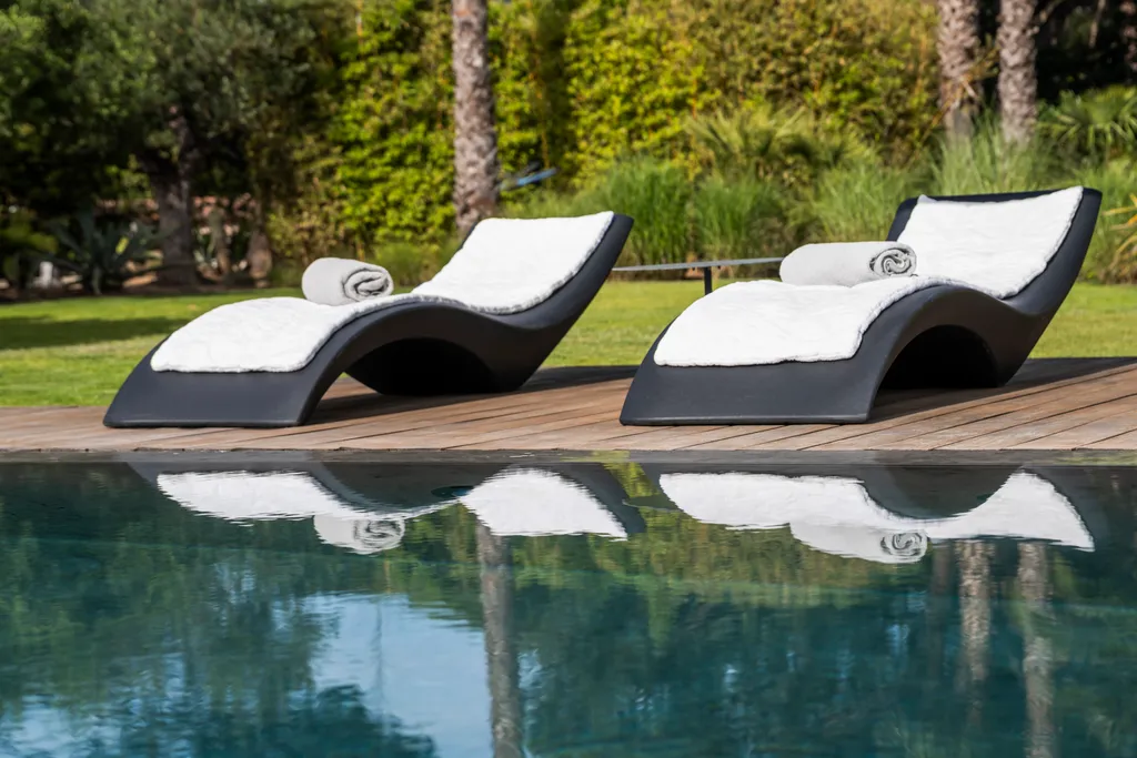 Two sculptural loungers with rolled towels mirrored in the still pool