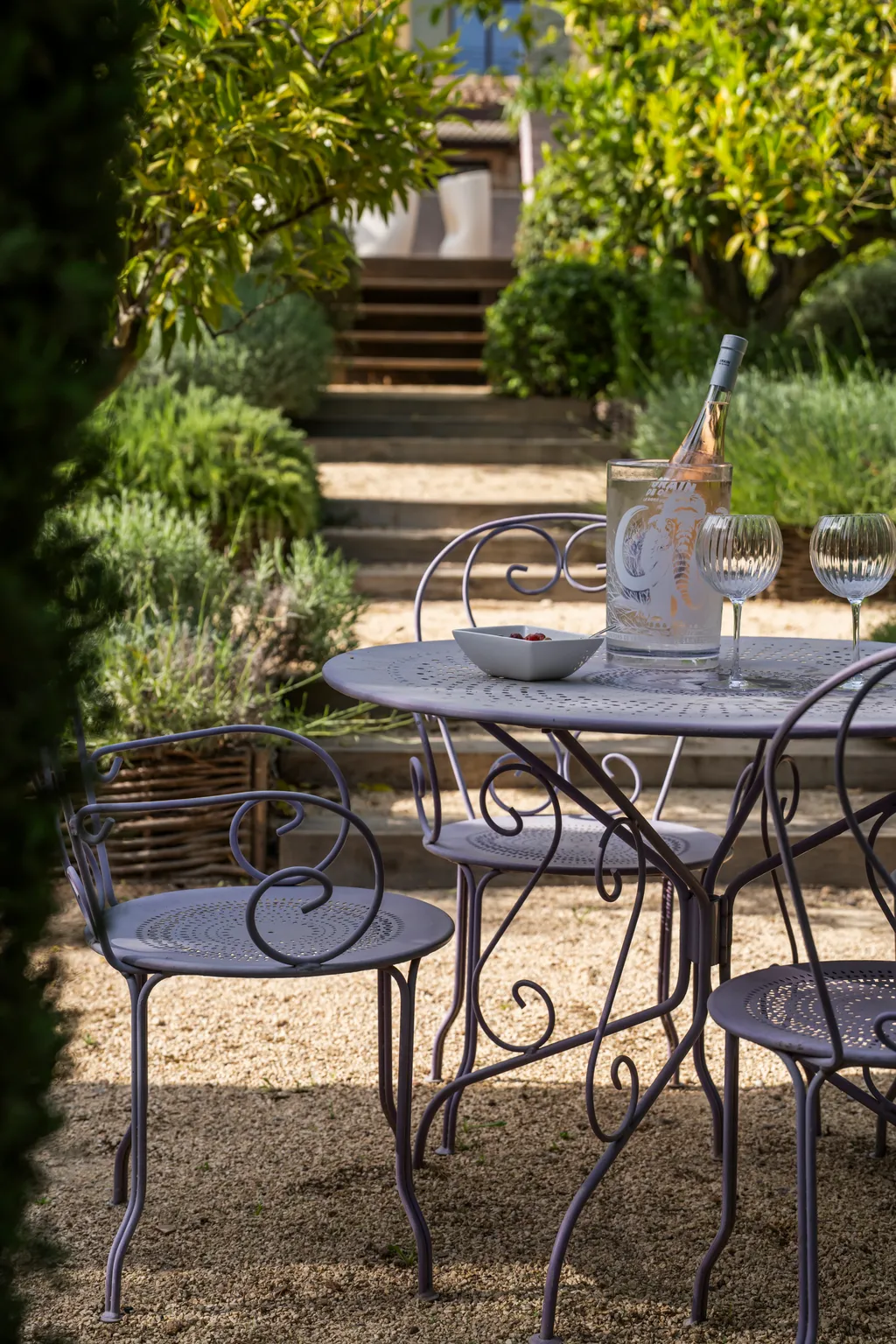 An iron garden table on gravel, steps climbing to the villa through lavender