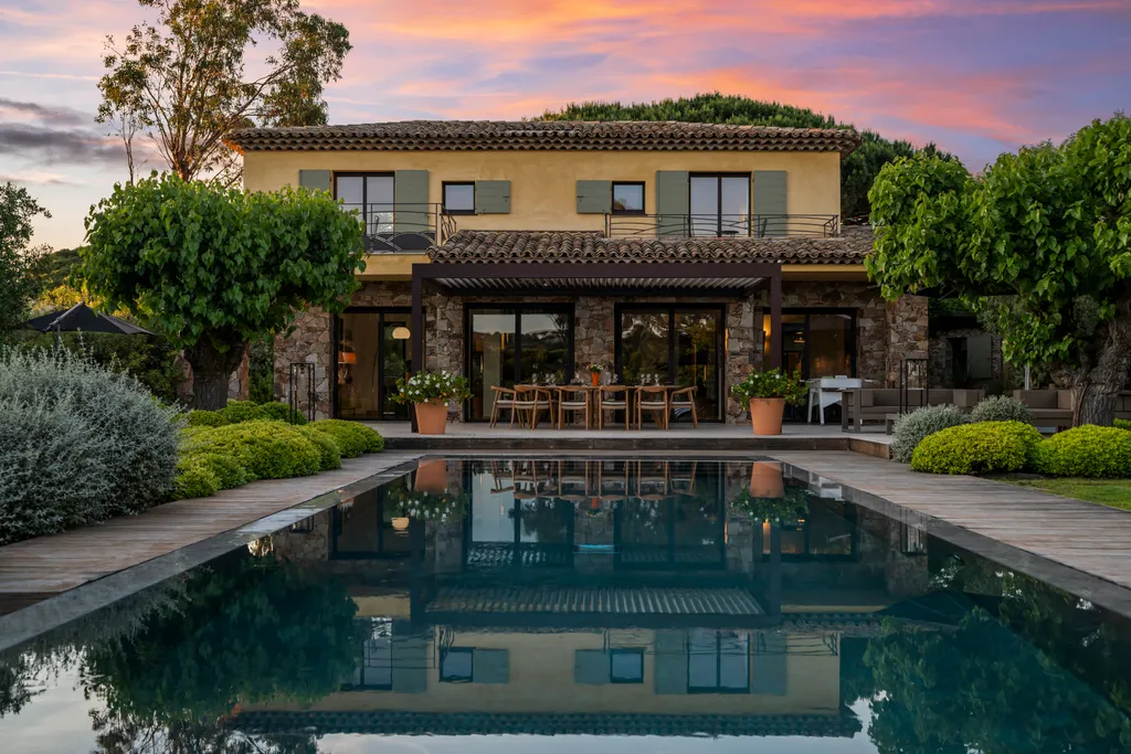 The villa at twilight, its lit loggia and pink sky mirrored in the pool