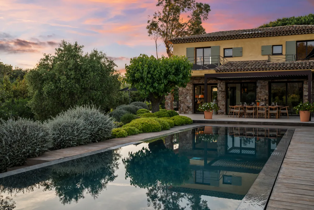 The villa's lit loggia beneath a pink twilight sky, reflected in the pool