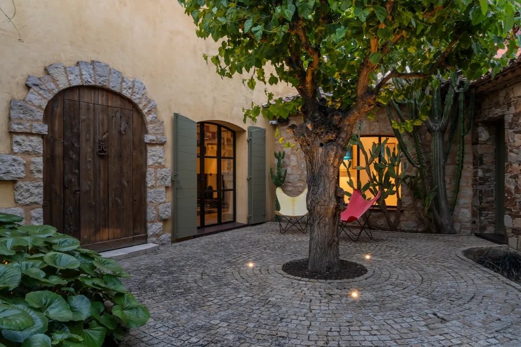 The enclosed courtyard at dusk — an old arched door, stone walls and an uplit tree