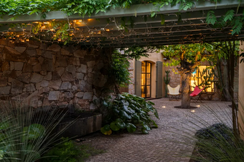 The courtyard at dusk, string lights glowing along a stone-and-vine pergola