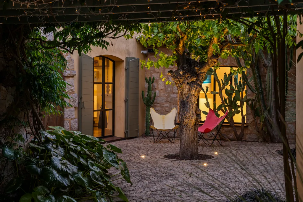 Butterfly chairs beneath an uplit tree in the cobbled courtyard at dusk