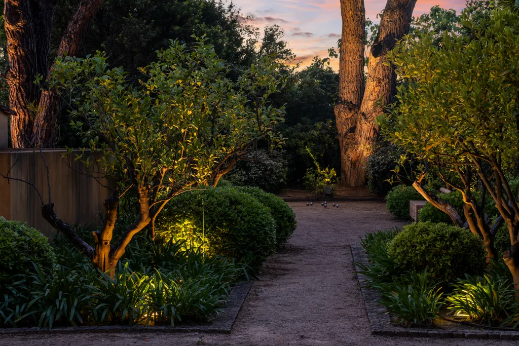 A garden path at dusk, its trees and borders picked out by warm uplighting