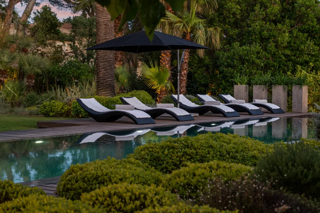 A row of loungers along the pool at dusk, mirrored in the water