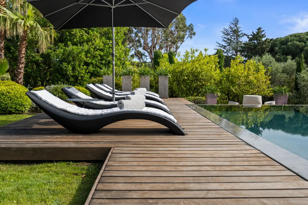 Black loungers with towels on the pool's timber deck under a parasol