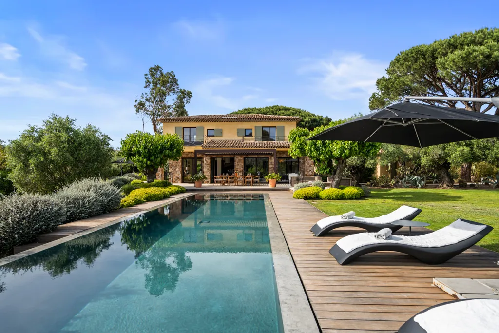 The villa, terrace and pool on a bright day, a parasol shading the deck