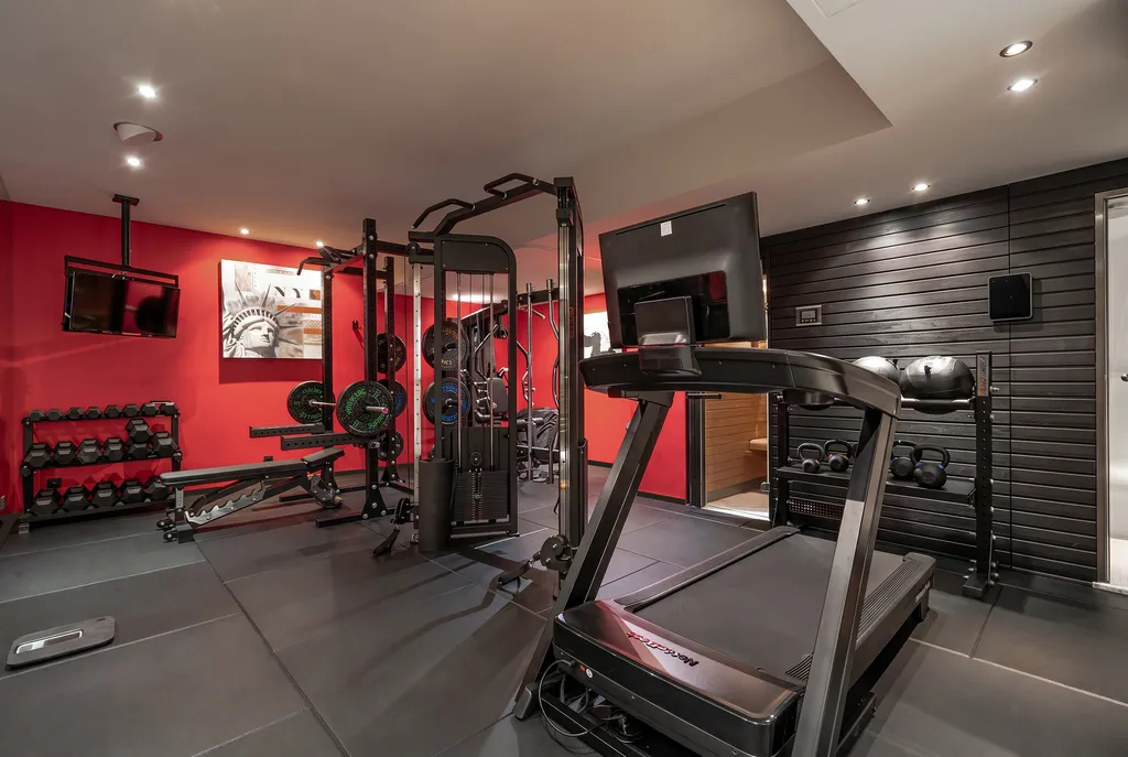 The gym, its treadmill and weights against a red feature wall